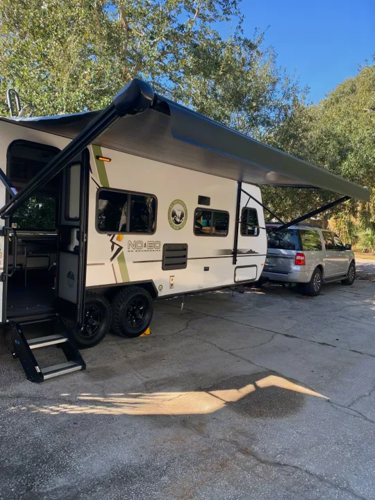 This RV rental is set up at a sunny campsite with its awning out, ready for adventure. A silver SUV is parked nearby.. Forest River no boundaries 2020