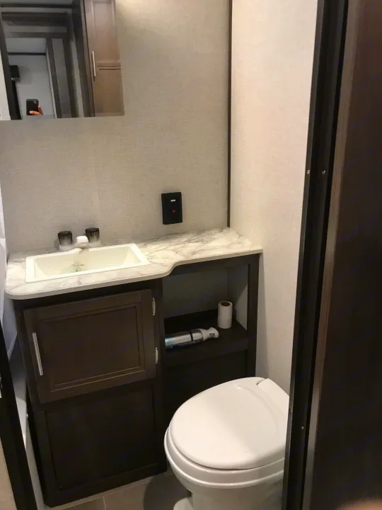 Inside an RV rental: a clean, compact bathroom featuring a sink, toilet, vanity, and mirror setup.. Coleman 295QB 2021