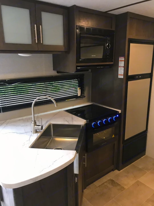 Step into this RV rental's modern kitchen with dark cabinets, a white countertop, microwave, stove, and fridge.. Coleman 295QB 2021