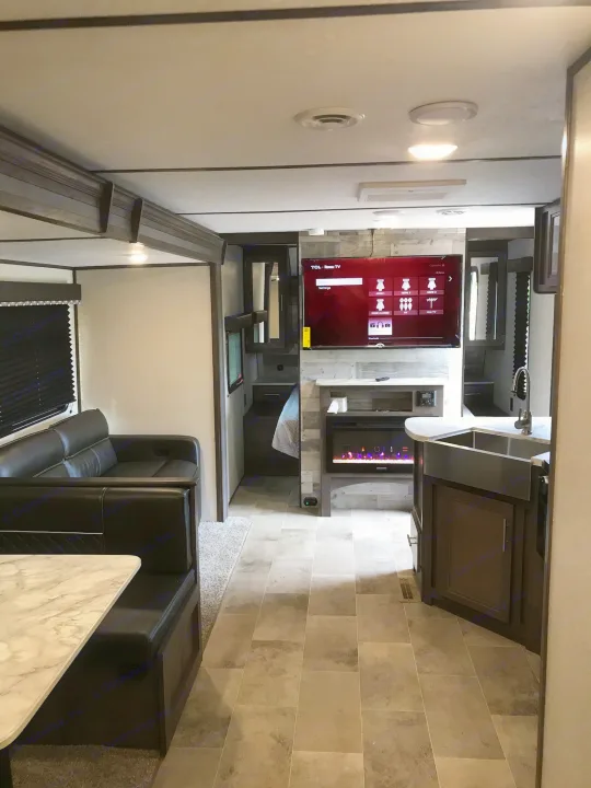 Experience comfort in this RV rental! Interior view of a living space, kitchen, dining booth, TV, and electric fireplace.. Coleman 295QB 2021