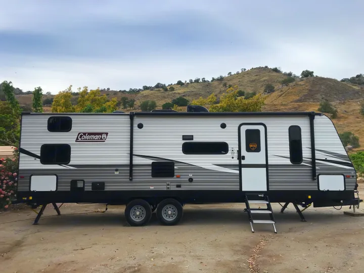 Rent this Coleman travel trailer RV. Parked on dirt with hills, ideal for camping adventures.. Coleman 295QB 2021