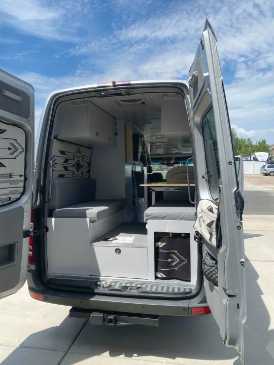 Rear view of a modern RV rental camper van with open doors, revealing its organized interior: seating, table, storage.. Dodge Sprinter 2500 170ext 2008