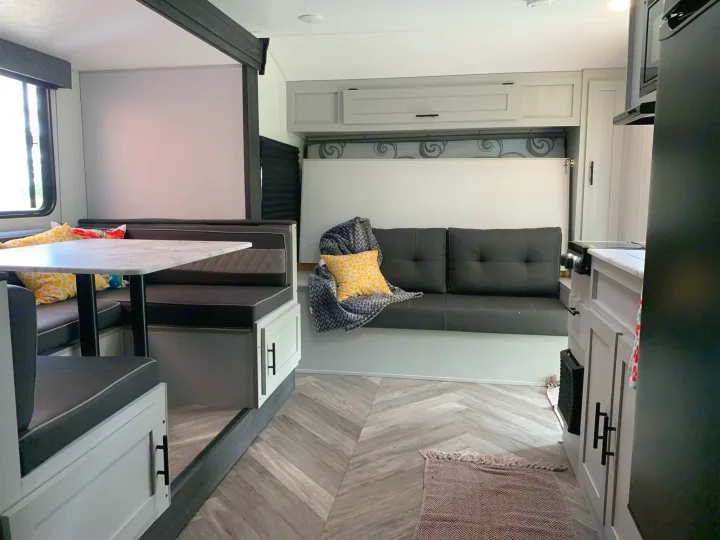 Inside a stylish rv rental: dinette, sofa, and clever fold-away bed. Light, modern interior with herringbone floor.. Forest River Salem 2021
