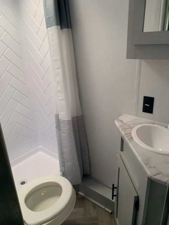 Clean, compact RV rental bathroom with white herringbone shower, toilet, and sink vanity.. Forest River Salem 2021