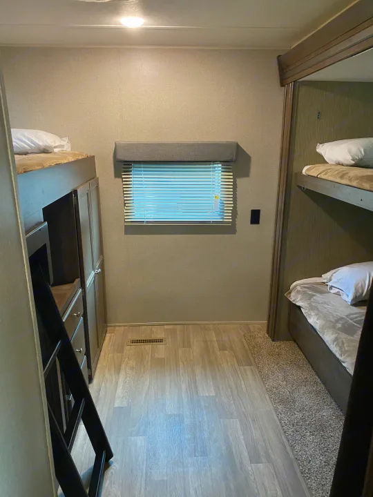 RV rental interior: A bright bunk room featuring stacked beds, a window with blinds, and integrated storage with a ladder.. Dutchmen Coleman 2019
