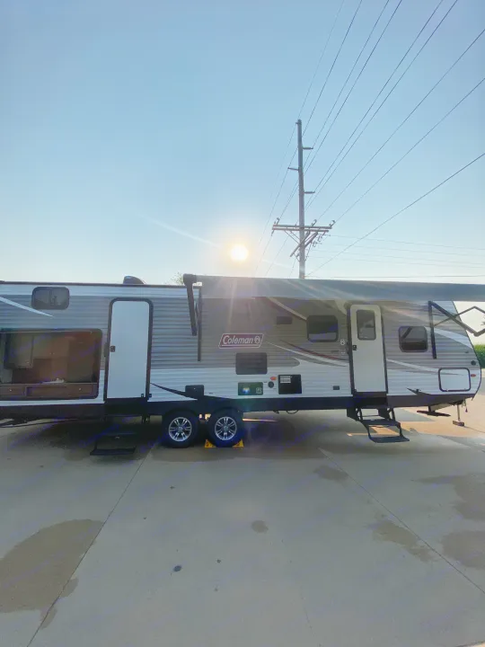 Spacious Coleman travel trailer, ready for your RV rental adventure. Parked on concrete with open doors and an extended awning under a sunny sky.. Dutchmen Coleman 2019