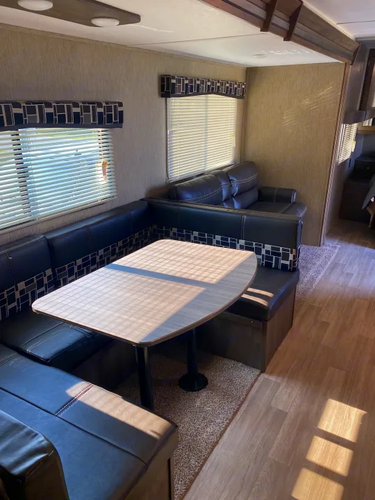 Modern RV rental interior: U-shaped dinette, dark leather sofa, and sunny windows.. Dutchmen Coleman 2019