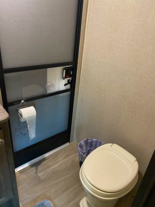 Inside an RV rental bathroom: light walls, wood-look floor, compact toilet, and a door with a toilet paper holder.. Dutchmen Coleman 2019