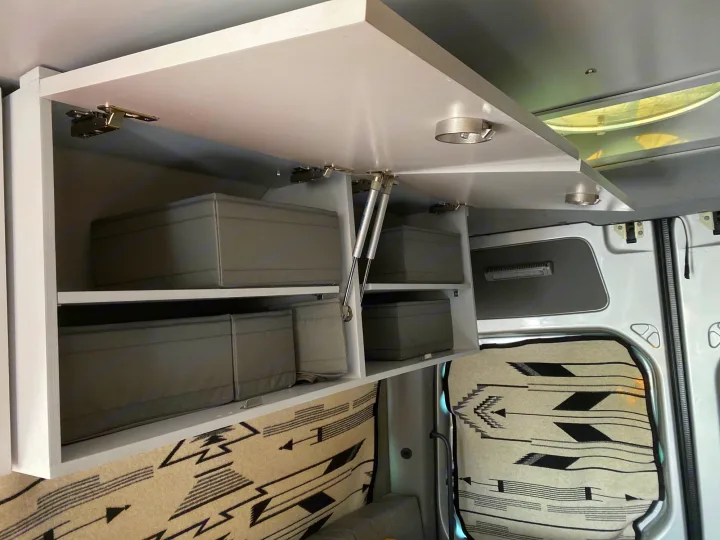 Open overhead cabinet with gray storage bins inside an RV rental, held up by gas struts for easy access and organization.. Dodge Sprinter 2500 170ext 2008