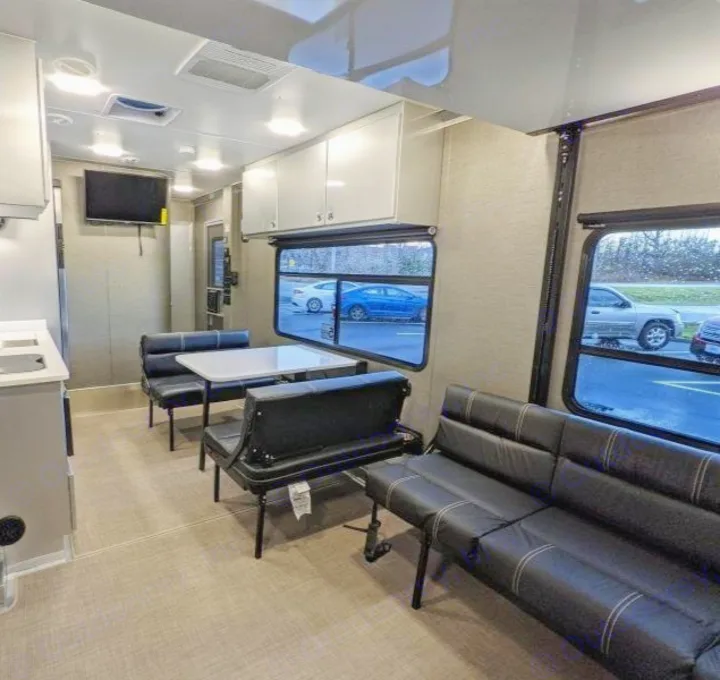 Spacious RV rental interior with convertible black leather seating, dining table, and kitchen for travel comfort.. Aluminum Trailer Company 2816 2021