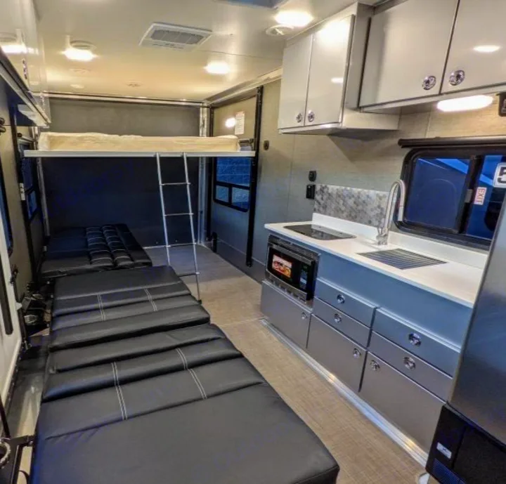 Explore this RV rental interior: upper bunk with ladder, lower convertible beds, & a compact kitchen area.. Aluminum Trailer Company 2816 2021