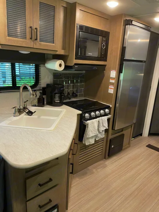 Modern RV rental kitchen with stainless steel appliances, spacious counter, sink, and stylish cabinets. Perfect for mobile living.. Keystone Hideout 2021
