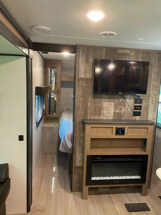 Inside a stylish rv rental: living area with TV, fireplace, and hallway glimpse to a cozy bedroom.. Keystone Hideout 2021