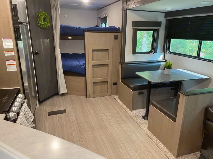Cozy rv rental interior with bunk beds, a dinette, and kitchen area, perfect for a family trip.. Keystone Hideout 2021