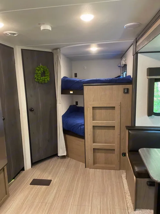 Inside an RV rental: view of neat bunk beds, compact dining area, and modern wood-look interior for comfortable travels.. Keystone Hideout 2021