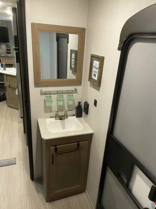 RV rental interior: a compact bathroom with light walls, sink vanity, mirror, and hanging storage. Perfect for travel.. Keystone Hideout 2021