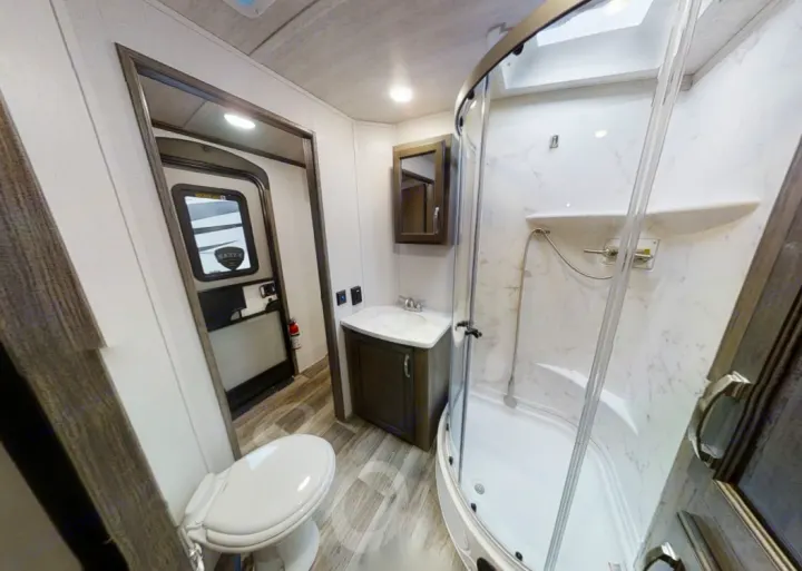 Explore this bright RV rental bathroom: a compact space with a toilet, sink vanity, and curved glass shower stall.. Keystone Cougar Half-Ton 2021
