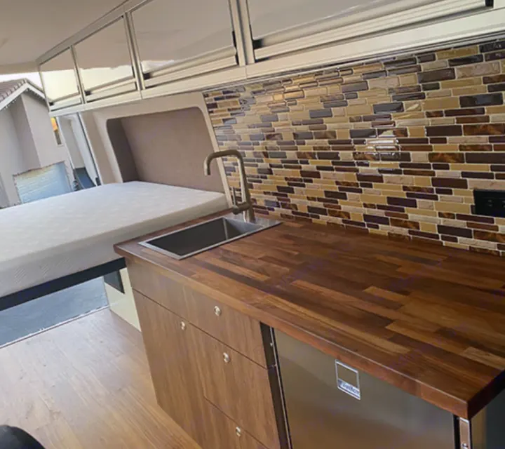 See this RV rental's clever interior: a modern kitchen with wood counters, sink, tiled backsplash, and a space-saving bed for travel.. Mercedes-Benz Sprinter 2020