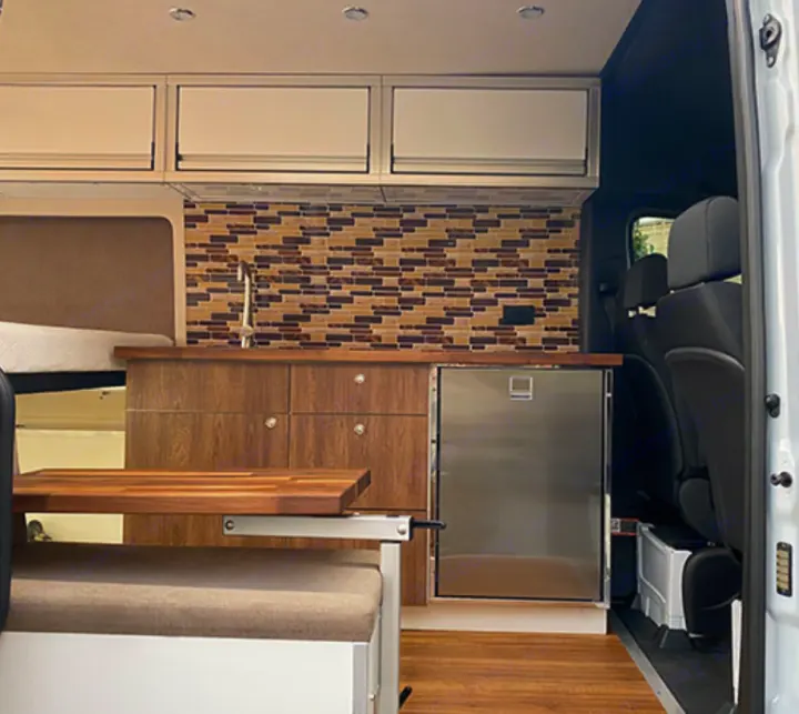 Modern camper van rv rental interior: kitchenette, fridge, wood cabinets, bench, and bed. Ready for adventure!. Mercedes-Benz Sprinter 2020