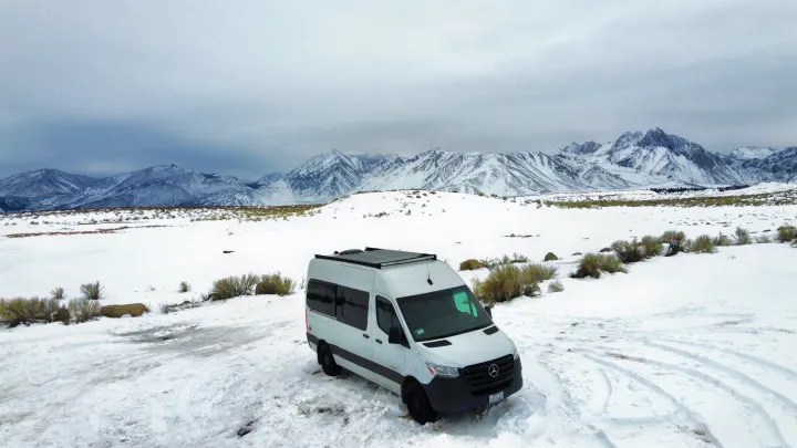 A white rv rental van braves a snowy mountain landscape under an overcast sky, perfect for winter travel.. Mercedes-Benz Sprinter 2020