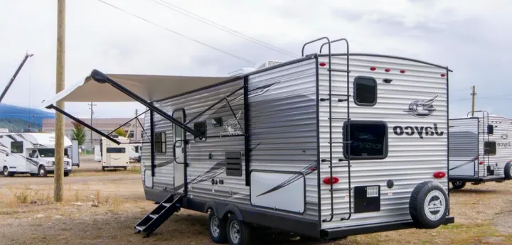 Featured RV rental: a silver travel trailer with extended awning, steps, and rear ladder. Many RVs on lot.. Jayco Jay Flight 2021