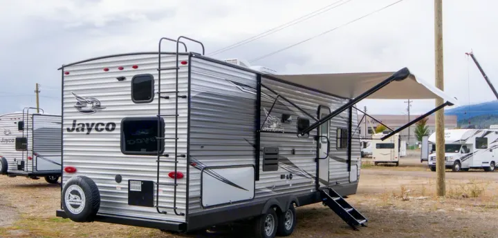 Jayco travel trailer for RV rental or sale, with an extended awning at a dealership lot, ready for outdoor adventures.. Jayco Jay Flight 2021