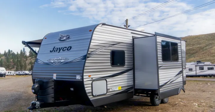 This Jayco travel trailer, a great option for RV rental, features an extended slide-out and partial awning on a gravel lot.. Jayco Jay Flight 2021