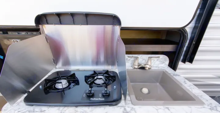 Outdoor kitchen in an RV rental, featuring a two-burner Suburban stove, sink, and marble-patterned countertop.. Jayco Jay Flight 2021