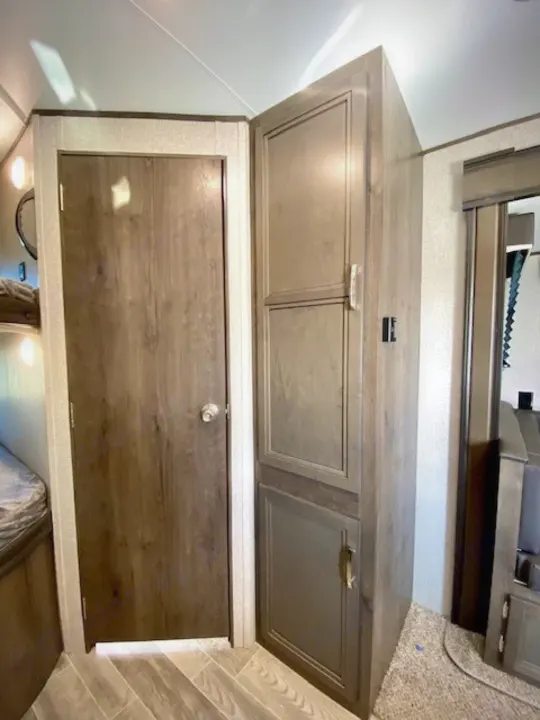 Inside an RV rental: a wood-grain door, corner storage cabinet, and bedroom glimpse. Compact living space.. Jayco Jay Flight 2021