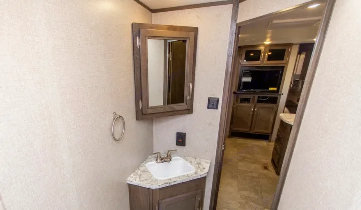 Inside an RV rental: a compact bathroom featuring a corner sink, mirrored medicine cabinet, and a view into the living area.. Jayco Jay Flight 2021