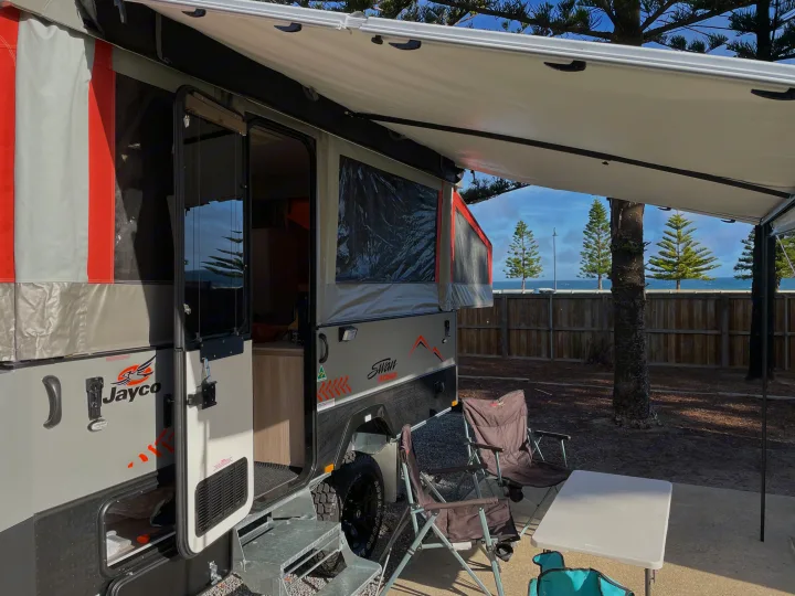 RV rental setup with extended awning, outdoor seating, and ocean views at a sunny caravan park.. Jayco Swan Outback 2021