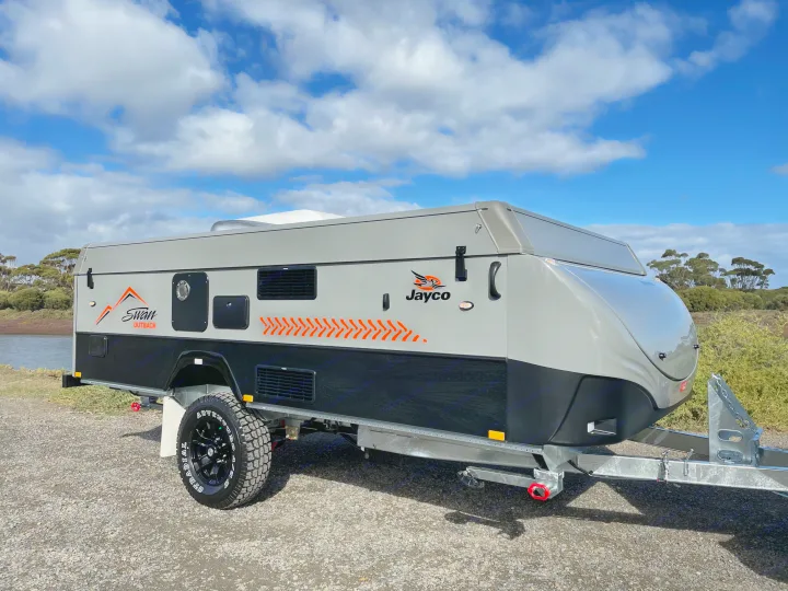 Ready for adventure: This modern grey and black Jayco travel trailer, ideal for RV rental, is set by the water under cloudy skies.. Jayco Swan Outback 2021