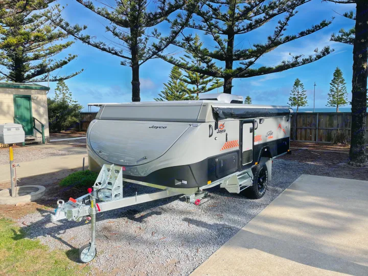 Jayco Swan Outback pop-top RV rental ready for adventure. This grey and black camper is parked at a sunny site near the ocean.. Jayco Swan Outback 2021