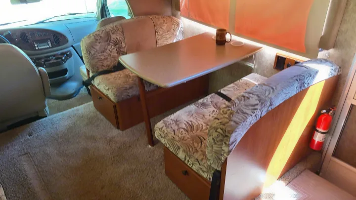 Interior view of an RV rental showing the dinette, front cabin, and safety equipment like a fire extinguisher. Ready for your journey.. Itasca Spirit 2007