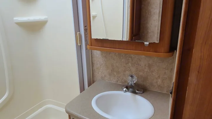 Compact RV rental bathroom featuring a white sink, chrome faucet, mirrored medicine cabinet, and integrated shower stall.. Itasca Spirit 2007