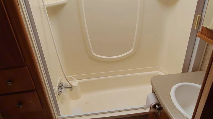 Clean and functional RV rental bathroom featuring a compact shower/tub combo and a small sink with a toilet paper holder.. Itasca Spirit 2007