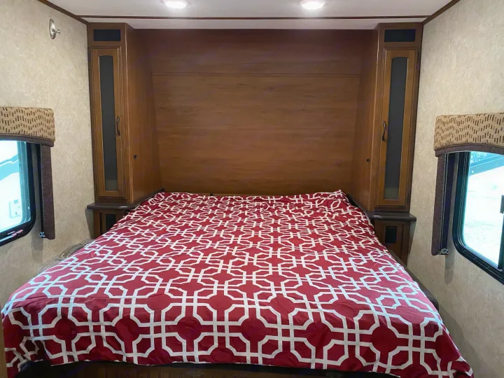 Spacious RV rental bedroom featuring a queen bed with a vibrant red and white duvet, built-in side cabinets, and large windows.. Jayco Jay Feather 2017