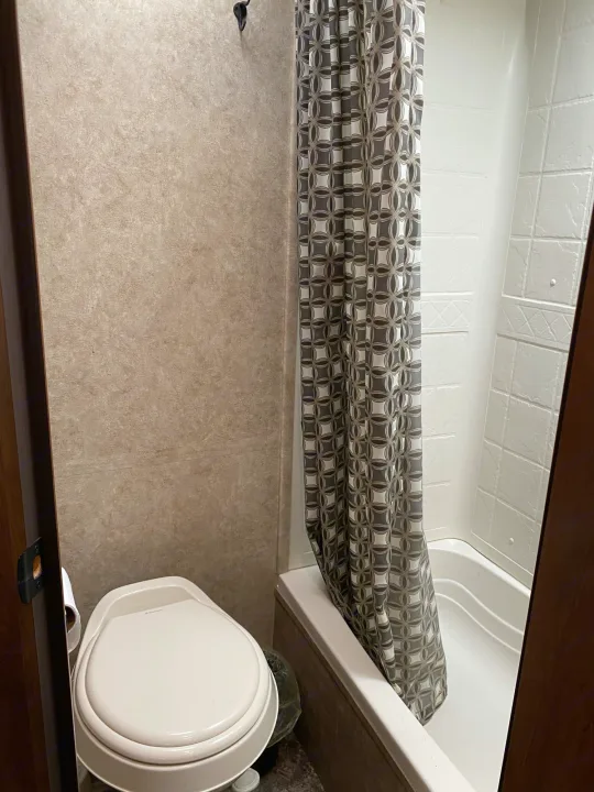 RV rental bathroom, featuring a compact toilet and a shower/tub with a grey geometric patterned curtain.. Jayco Jay Feather 2017