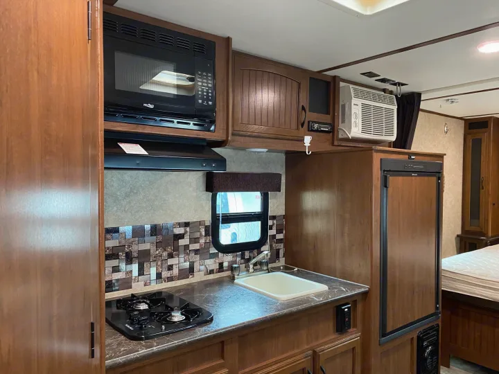 RV rental interior showcasing a compact kitchen with stove, microwave, sink, fridge, and AC.. Jayco Jay Feather 2017