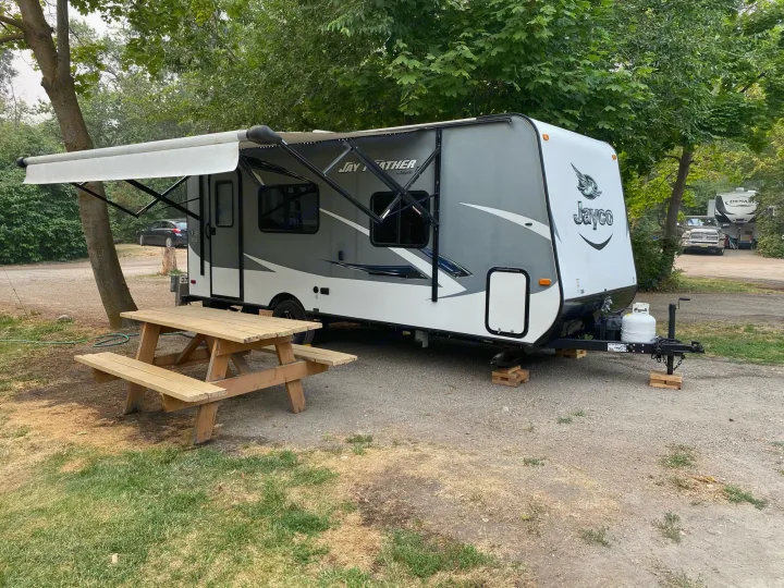 A grey and white Jayco Jay Feather RV rental parked at a shady campsite with a wooden picnic table.. Jayco Jay Feather 2017