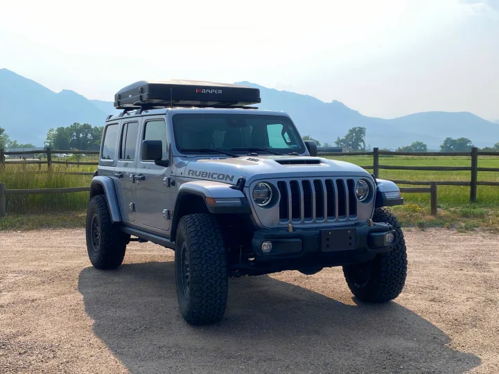 Silver Jeep Wrangler Rubicon with iKamper rooftop tent on a gravel path, ideal for an RV rental adventure in mountains.. Jeep Wrangler Unlimited Rubicon 392 2021