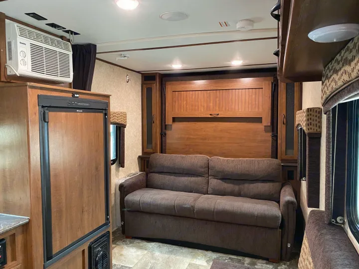 RV rental interior: living area with sofa, refrigerator, AC, and a wooden panel that hides a pull-down bed.. Jayco Jay Feather 2017