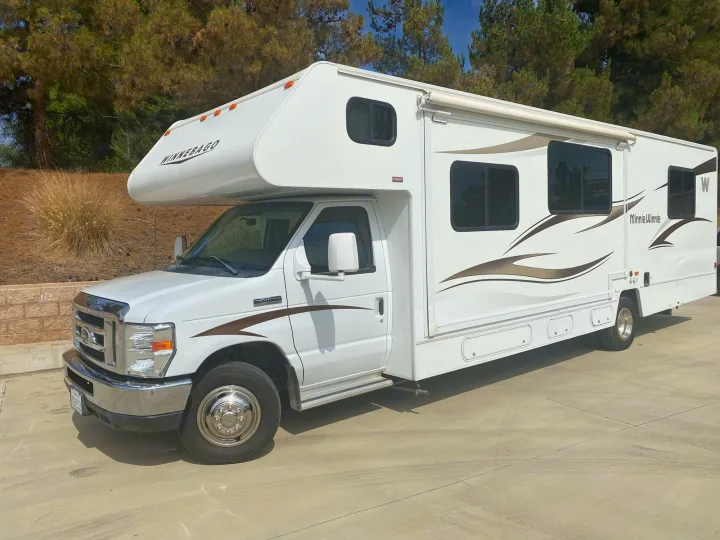 White Winnebago Minnie Winnie RV rental, with brown decals, parked on pavement under trees, ready for adventure.. Winnebago Minnie Winnie 2015