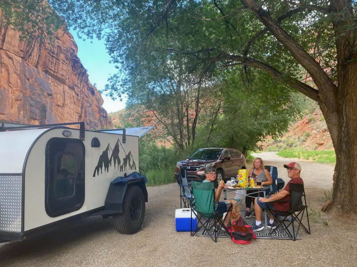 Four people enjoy an outdoor meal by their **RV rental** and SUV, with scenic cliffs and shady trees in the background.. Other Other 2021