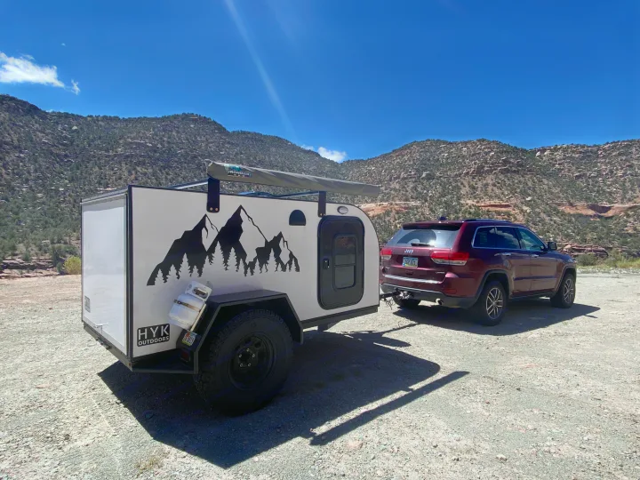 Adventure-ready RV rental: Teardrop trailer and SUV parked on a gravel road with scenic mountains, ideal for outdoor travel.. Other Other 2021