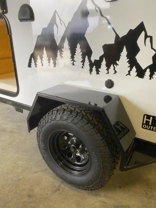 White RV rental travel trailer with mountain & tree decal, rugged off-road tire, and black fender detail.. Other Other 2021