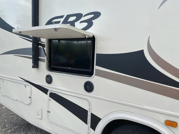 Side of an RV rental featuring an outdoor entertainment area with a TV, speakers, and storage below.. Forest River Forester 2018