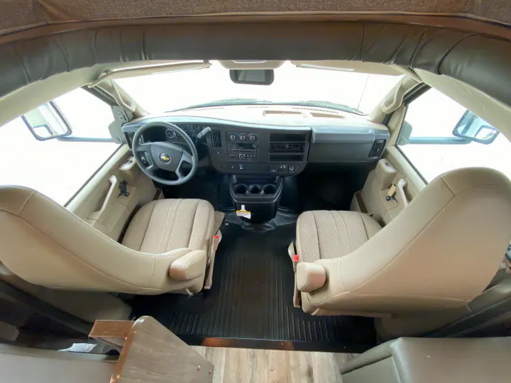 Detailed RV rental interior: spacious cockpit with tan seats, Chevrolet steering wheel, and dashboard.. Jayco Redhawk 27N 2022