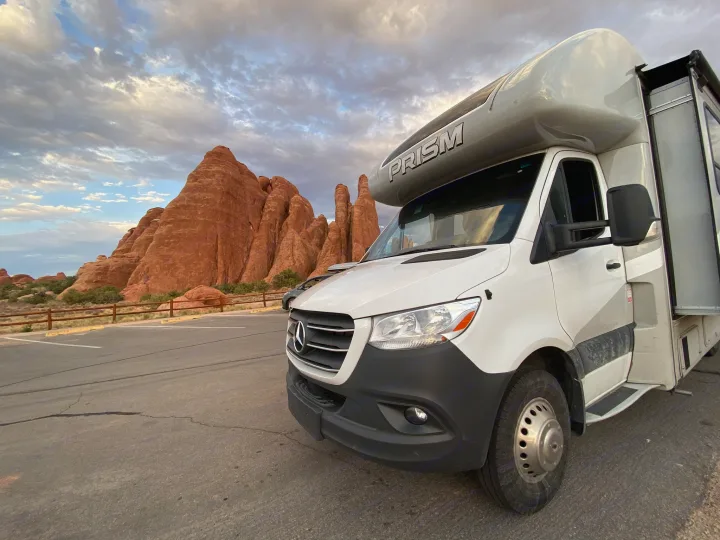 This rv rental motorhome is parked before stunning red rock formations & a cloudy sky, ideal for scenic park travel.. Mercedes-Benz Sprinter Coachmen Prism 2021