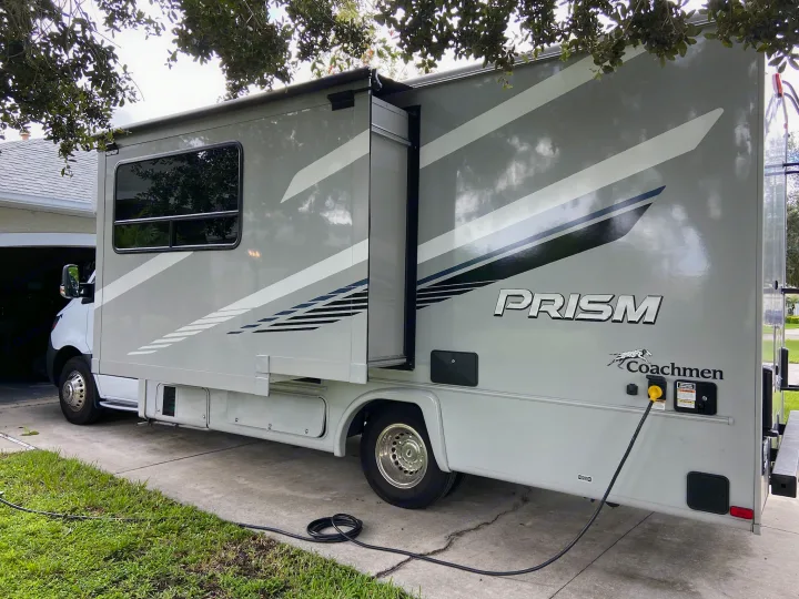 Grey Coachmen Prism RV, likely an rv rental, with slide-out extended. Power cord plugged in, parked on a driveway.. Mercedes-Benz Sprinter Coachmen Prism 2021